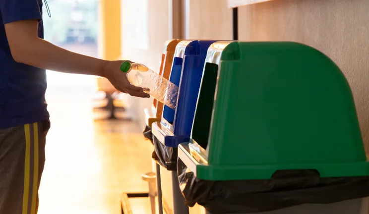 A person putting a plastic bottle into a recycling bin